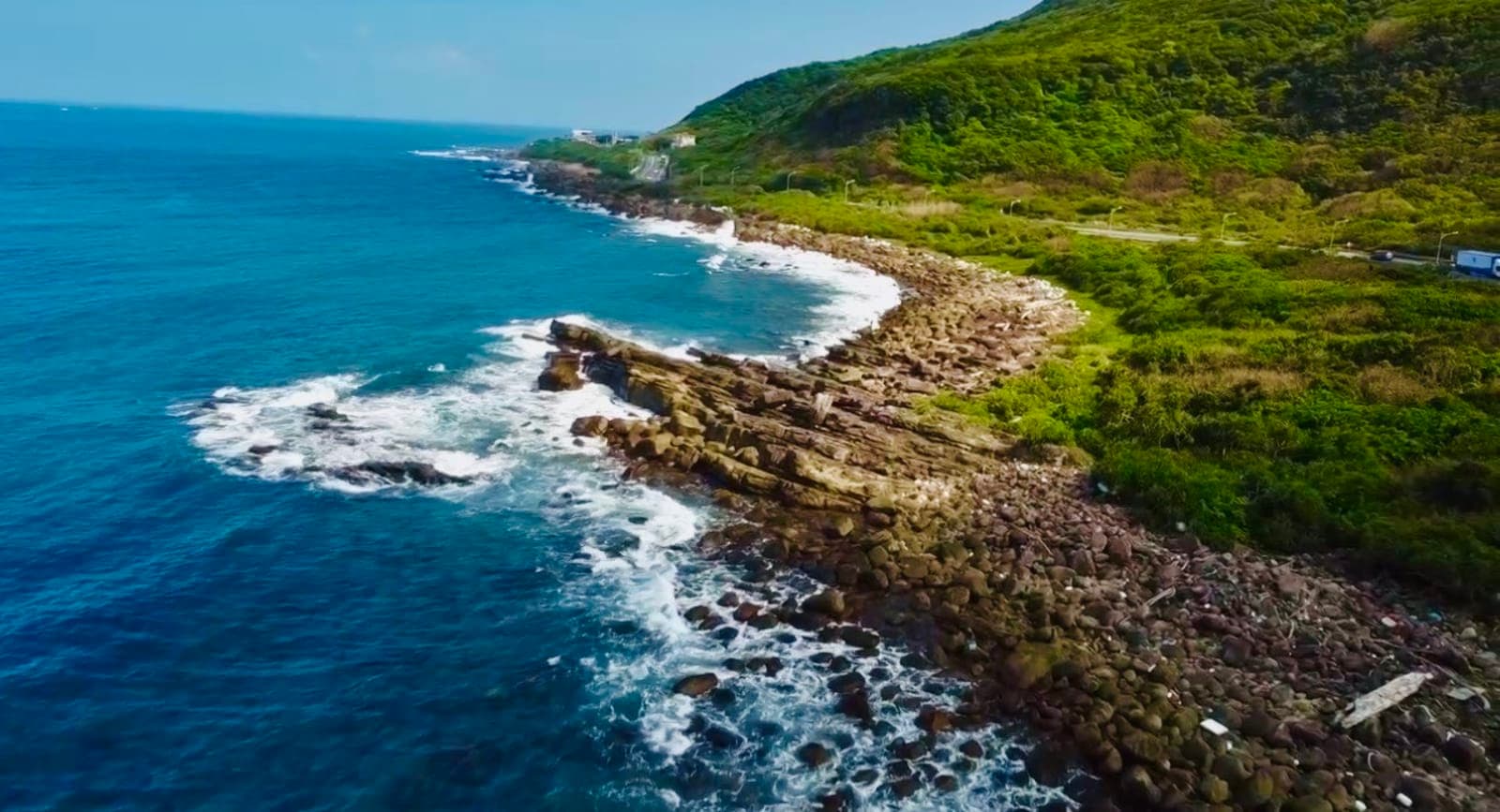 東北角岩岸與浪花航拍，翠綠山丘與蔚藍海面
